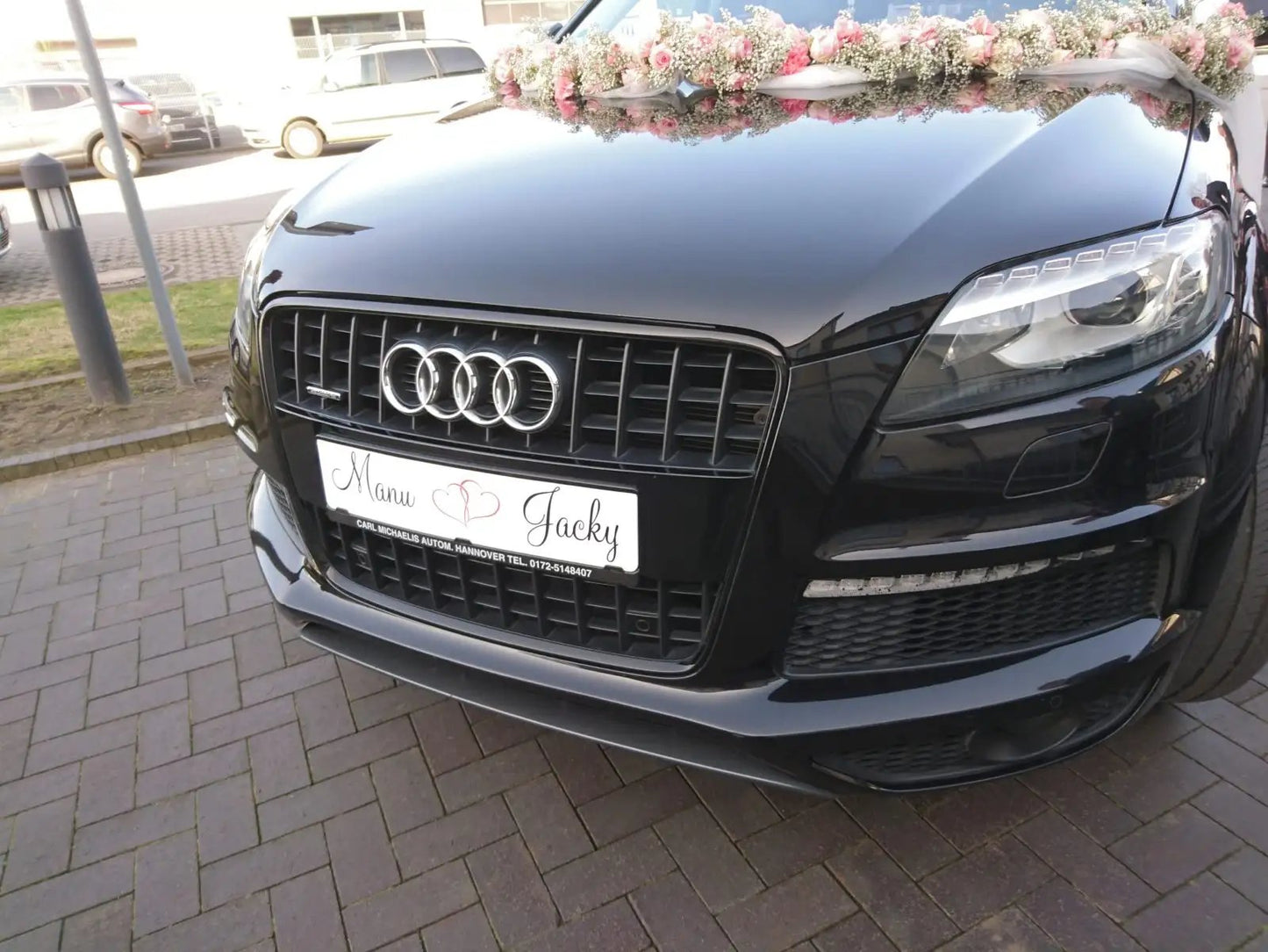 Front view of a wedding car with a floral decoration and personalized license plate on a black vehicle.