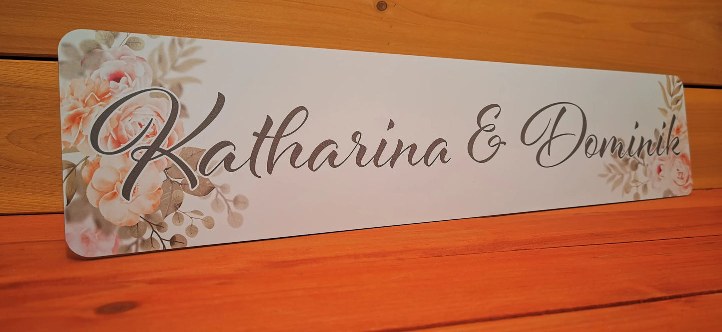 Elegantes Hochzeitsauto-Kennzeichen mit personalisiertem Schriftzug und floralen Motiven auf edlen Hintergrund.