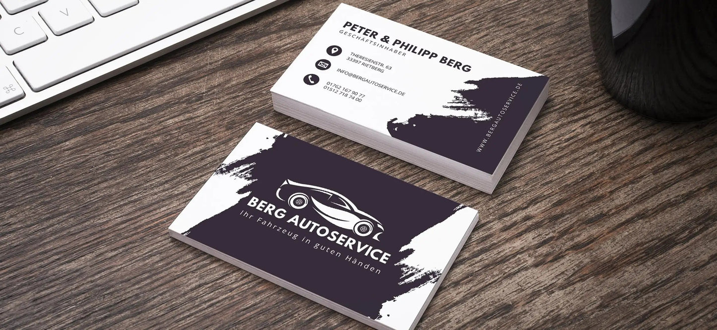 Stack of professionally designed business cards for Berg Autoservice placed on a wooden desk beside a keyboard, showcasing dual-side print.