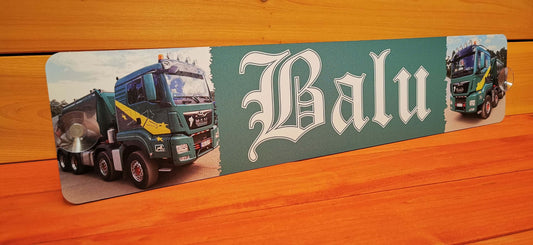 Decorative LKW Namensschild with 'Balu' text and truck images on wooden surface.