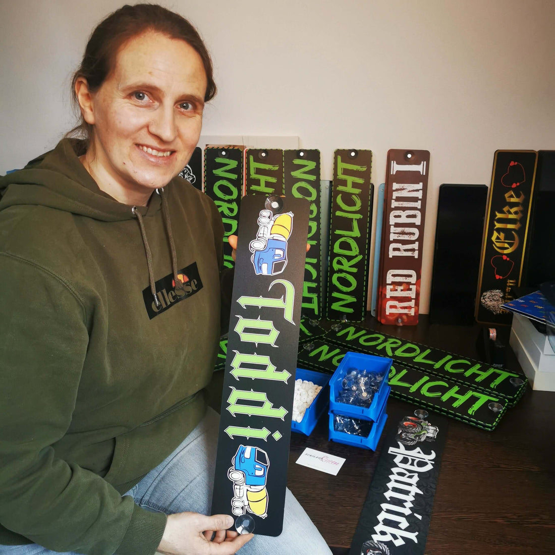 Person holding customized LKW Namensschild with Wunschmotiv design, surrounded by various name plaques on display.