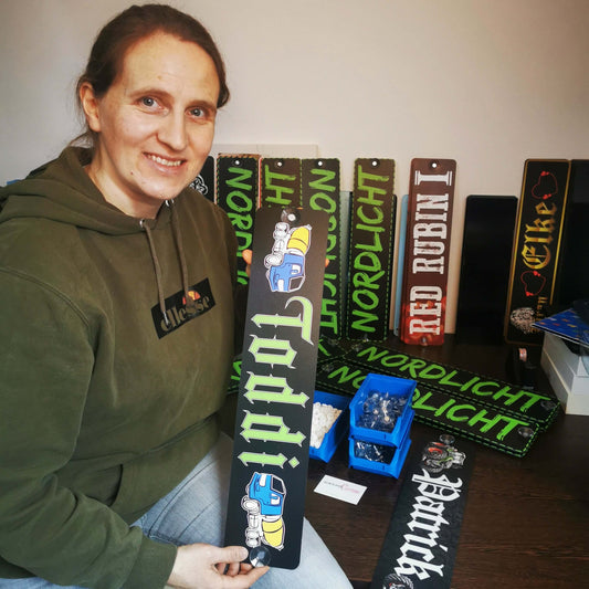 Person holding customized LKW Namensschild with Wunschmotiv design, surrounded by various name plaques on display.