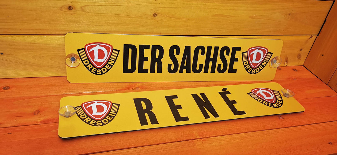 Custom LKW nameplates reading 'DER SACHSE' and 'RENÉ' on a wooden background, personalized by Swetlana - Die Schilderqueen.