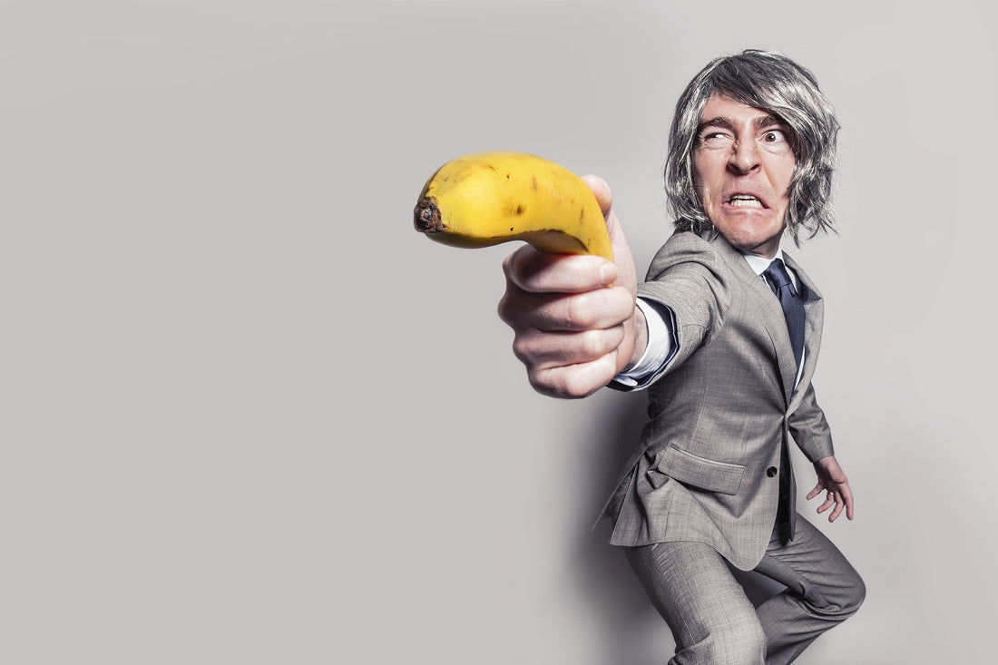 Man in a suit humorously posing with a banana as a weapon against a gray background.