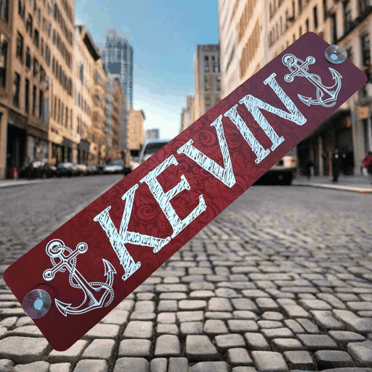 Red LKW-Namensschild "KEVIN" with anchor design on a cobblestone street, showcasing its durable aluminum construction and suction cup fittings.