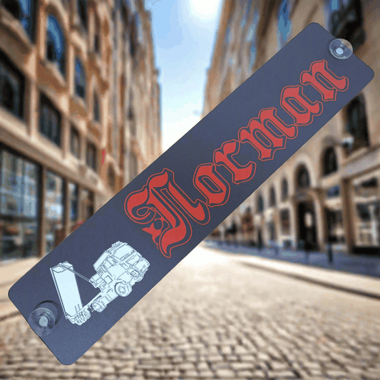 LKW-Namensschild "Norman" aus B-Ware mit rotem Schriftzug und Saugnäpfen, auf Alu-Verbundplatte in der Stadt.