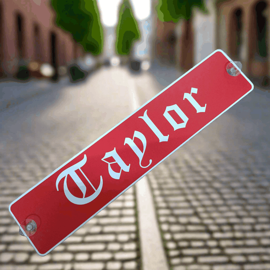 Red personalized LKW-Namensschild with 'Taylor' text, featuring suction cups for easy mounting on a cobblestone street background.