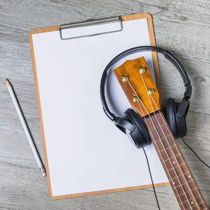 Clipboard with blank paper, pencil, guitar neck, and headphones, symbolizing creativity in music composition and songwriting.