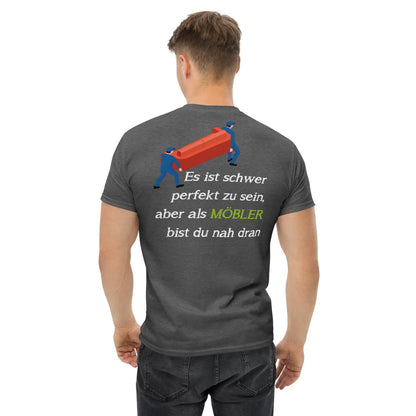 Mann trägt dunkelgraues Herren-T-Shirt mit MÖBLER Grafik und deutschem Slogan auf dem Rücken, hergestellt aus 100 % Baumwolle.