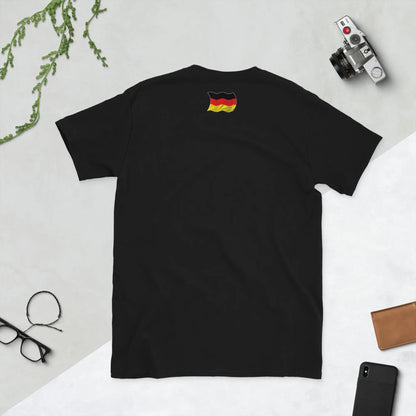 Back view of black unisex T-shirt with German flag design, laid flat with camera and accessories on light background.