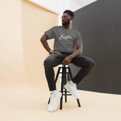 Man wearing "Erlebe Jesus Christus" T-Shirt, sitting on stool, black jeans and sneakers, casual studio setting.