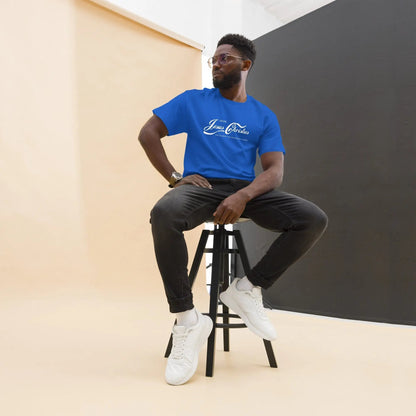 Man sitting on stool wearing a blue T-shirt with the text 'Jesus Christus' in a modern studio setting.