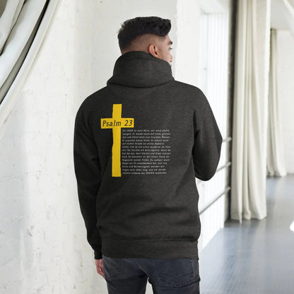 Person wearing a black hoodie with a yellow cross and Psalm 23 print on the back, standing in a minimalist interior.