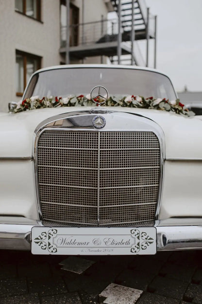 White vintage wedding car with personalized front license plate adorned with flowers.