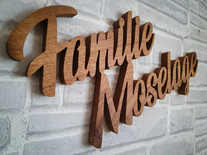 3D Echtholz Familienname in geschwungener Schrift an einer Steinwand, ideal für edle Innen- und Außengestaltung.