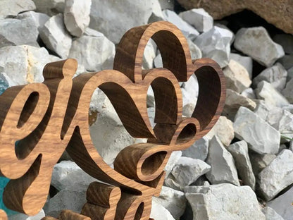 3D Familienname aus echtem Holz mit stilvollen Schriftzügen, robust für Außeneinsatz, gezeigt vor einem steinigen Hintergrund.