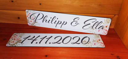 Hochzeitswagen-Autokennzeichen mit floralem Design, personalisiert mit Namen und Datum, auf Holzhintergrund.