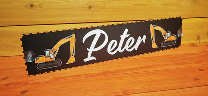 Custom LKW nameplate with white text 'Peter' and excavator design on black background, mounted on wooden surface.