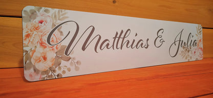 Personalized wedding car license plate with floral design, featuring names in elegant script on a wooden background.