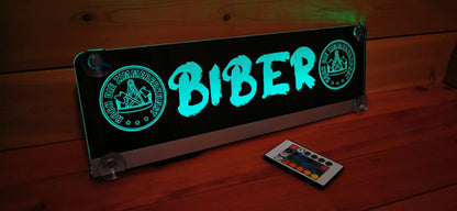 Illuminated LED truck nameplate with custom design, featuring suction cups and remote control, glowing on a wooden surface.