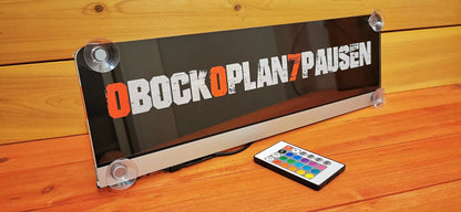 Illuminated LED truck nameplate with suction cups and remote control on wooden surface.
