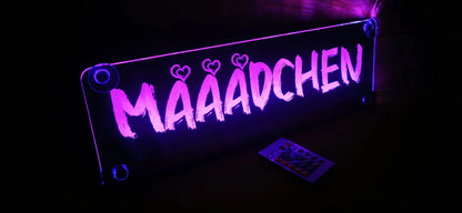 Illuminated LED truck nameplate with suction cups and custom text design "MÄÄÄDCHEN" in purple light.