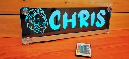 Custom LED truck nameplate with lion motif, blue lighting, remote control, suction cup mount on wooden background.