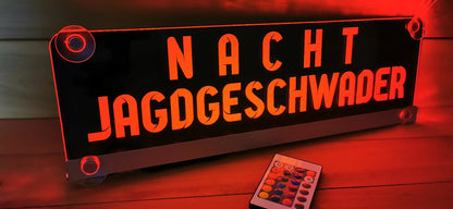 Illuminated LED truck nameplate 'Nacht Jagdgeschwader' with suction cups and remote control on wood surface.