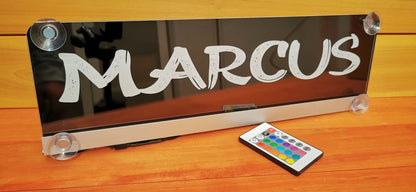 LED Namensschild für LKW mit Saugnapf und Wunschmotiv, zeigt Name 'Marcus' mit Fernbedienung zur Farbsteuerung, auf Holztisch.