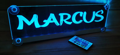 Illuminated LED truck nameplate with custom design and suction cups on display, remote control nearby.