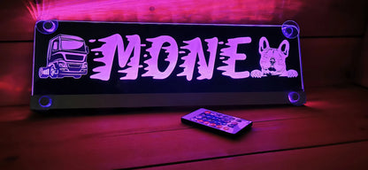 Illuminated LED truck nameplate with custom design, featuring a truck and dog graphic, remote control visible, glowing in purple light.