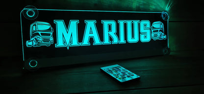Illuminated LED truck nameplate with suction cups and personalized motif, glowing in a dark setting next to a remote control.