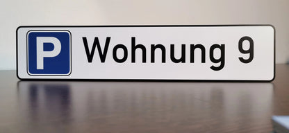 Aluminium parking sign with blue 'P' symbol and text 'Wohnung 9' on a wooden table.