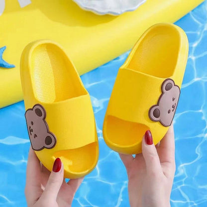 Yellow children's slippers for kids with bear design, held over a pool background for ultimate comfort and style.