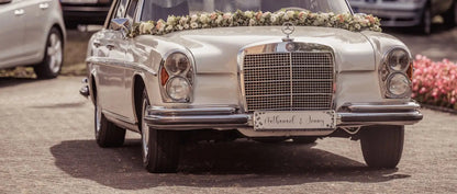 Elegant wedding car with personalized license plate and floral decorations for a stylish wedding photoshoot.